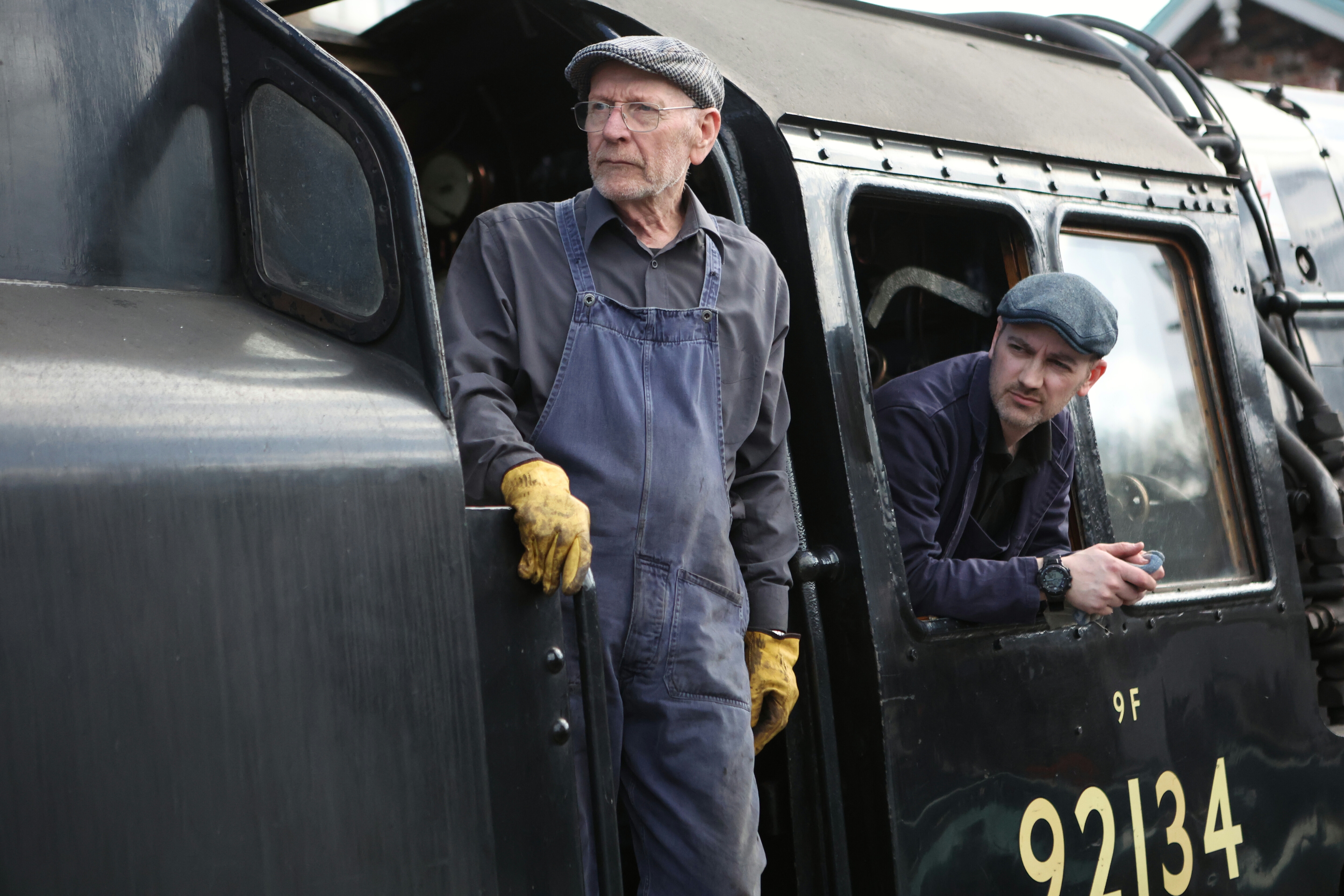 Locomotive footplate staff look out from the cab of a steam locomotive.