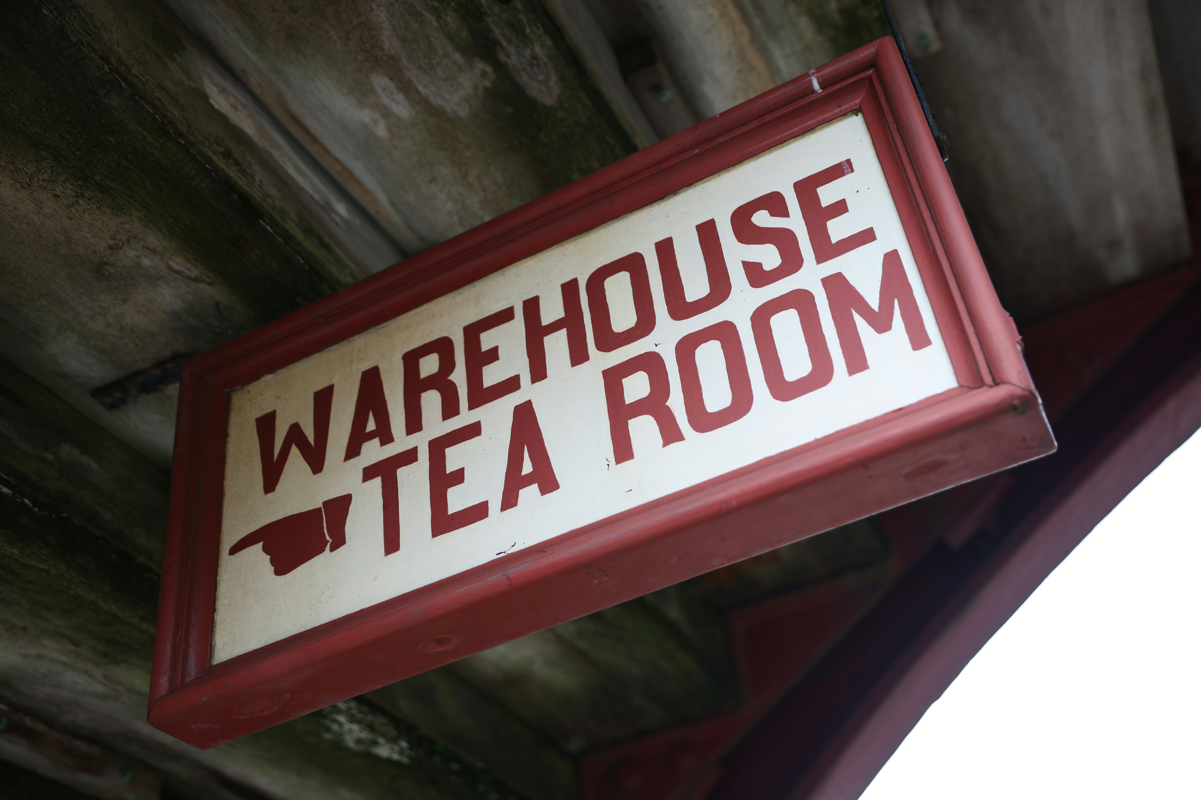 A hand-painted direction sign with the words 'Warehouse Tea Room' and a hand pointing left.
