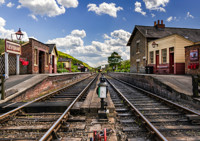 Levisham station in the sun, with a steam train departing in the distance.