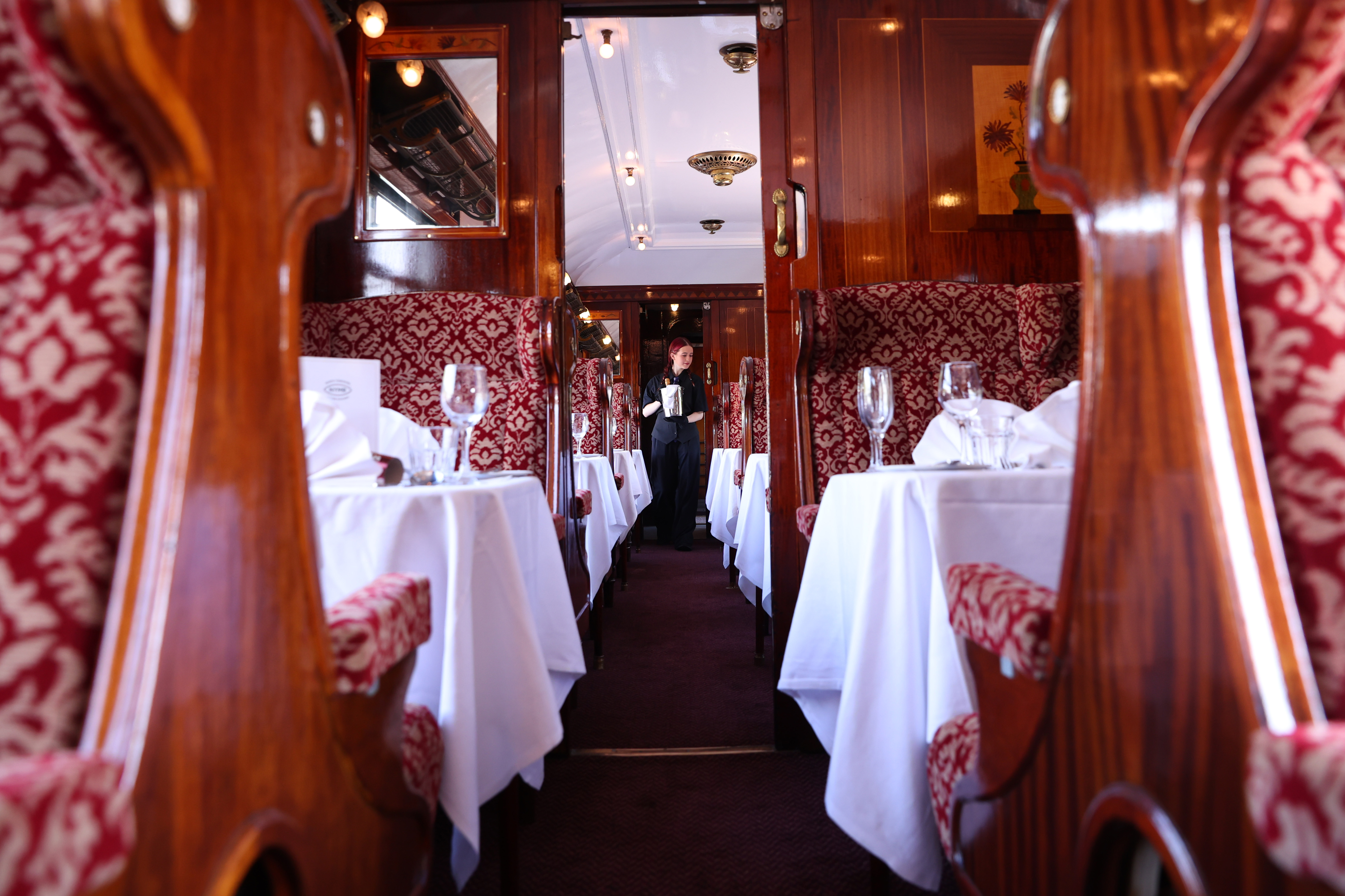 The inside of Car 79 set for dinner and including a waitress walking up the central aisle.