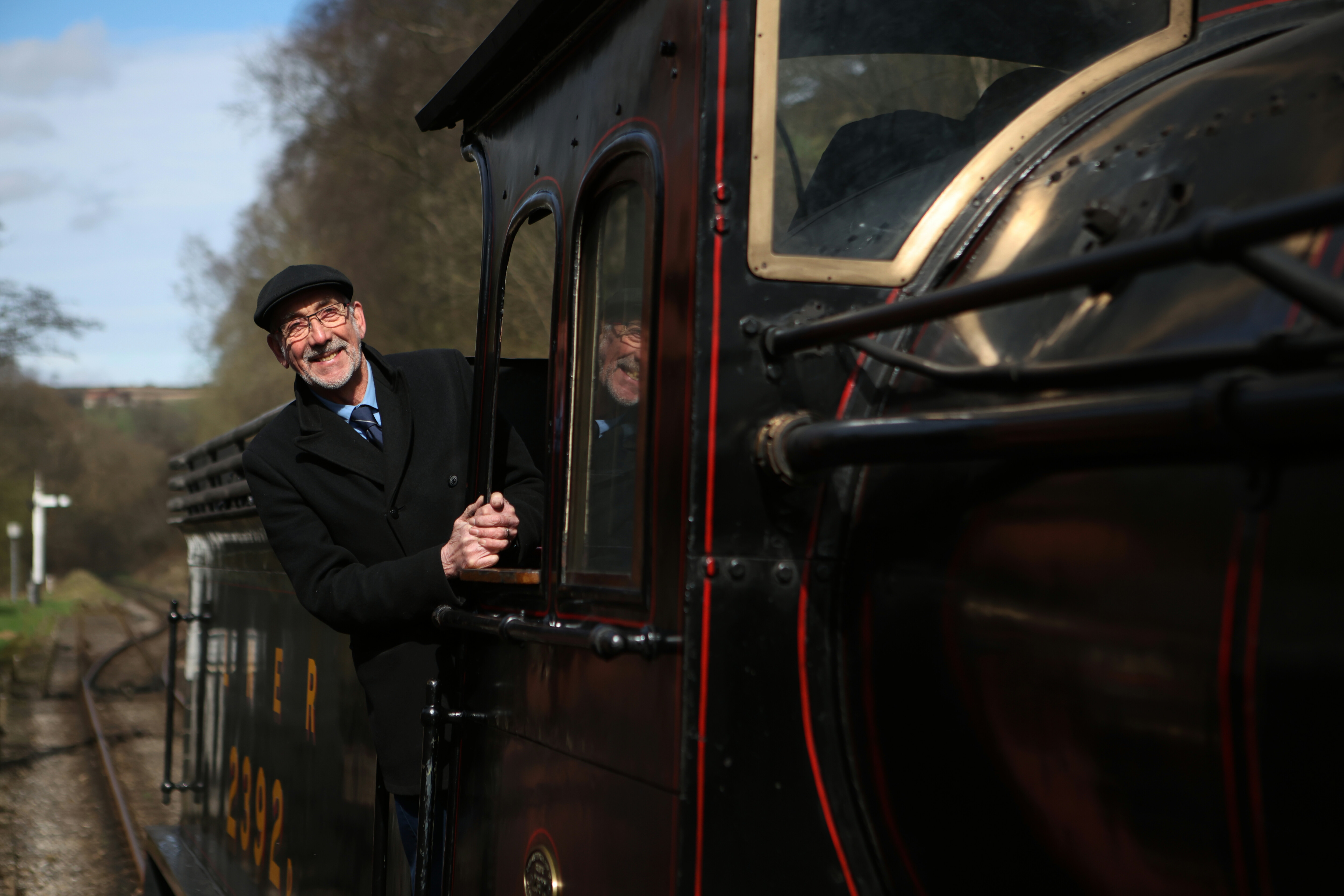 The driver of a steam locomotive looks out of the cab towards the camera.