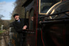The driver of a steam locomotive looks out of the cab towards the camera.