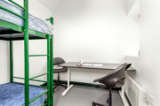 A bedroom at The Outstation with green bunk beds with blue mattresses and a desk with two chairs.