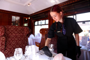 A waitress adjusting a wine glass on a table set for dinner in Car 79.