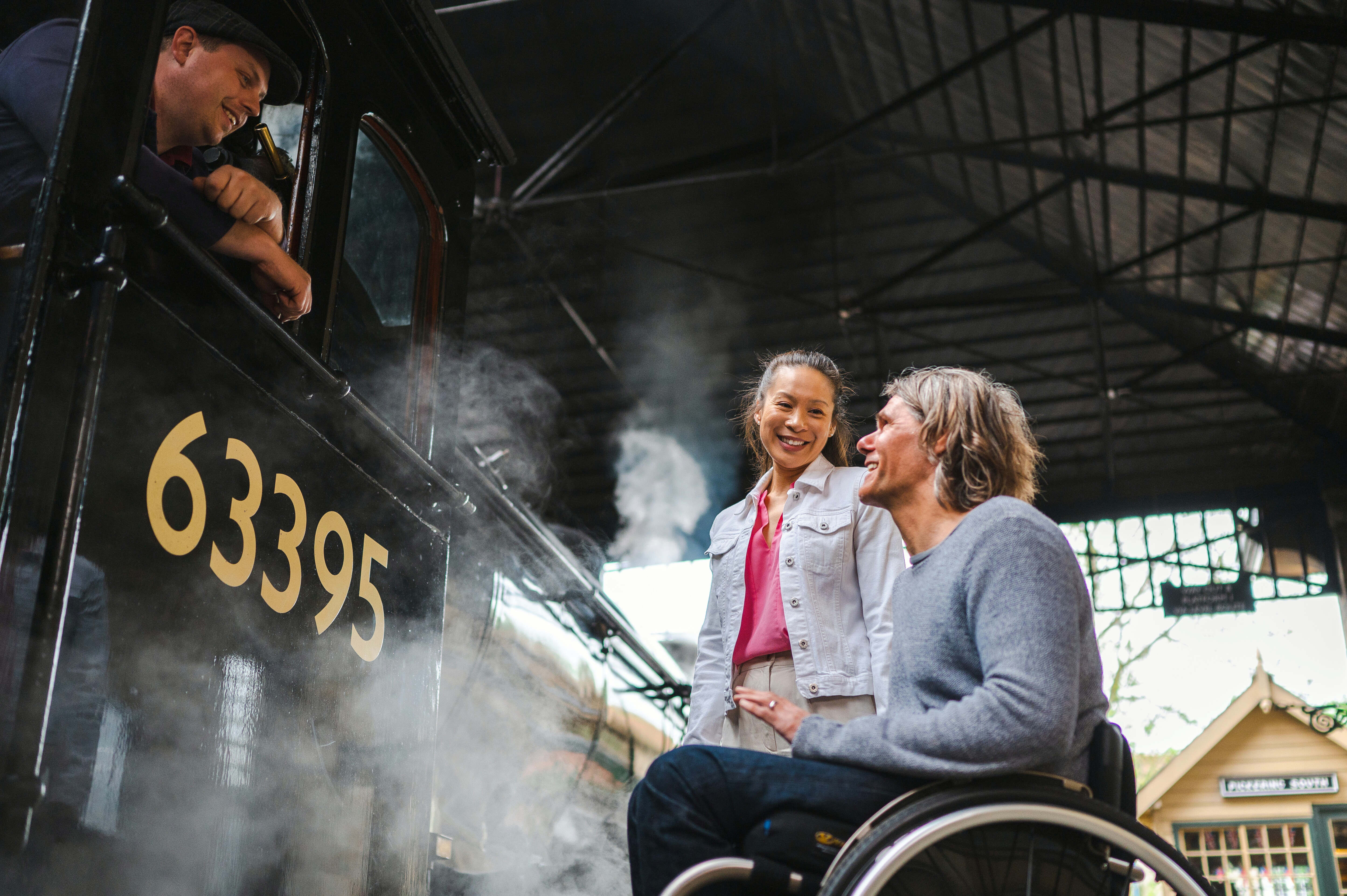 A man in a wheelchair looks up towards the locomotive footplate person.