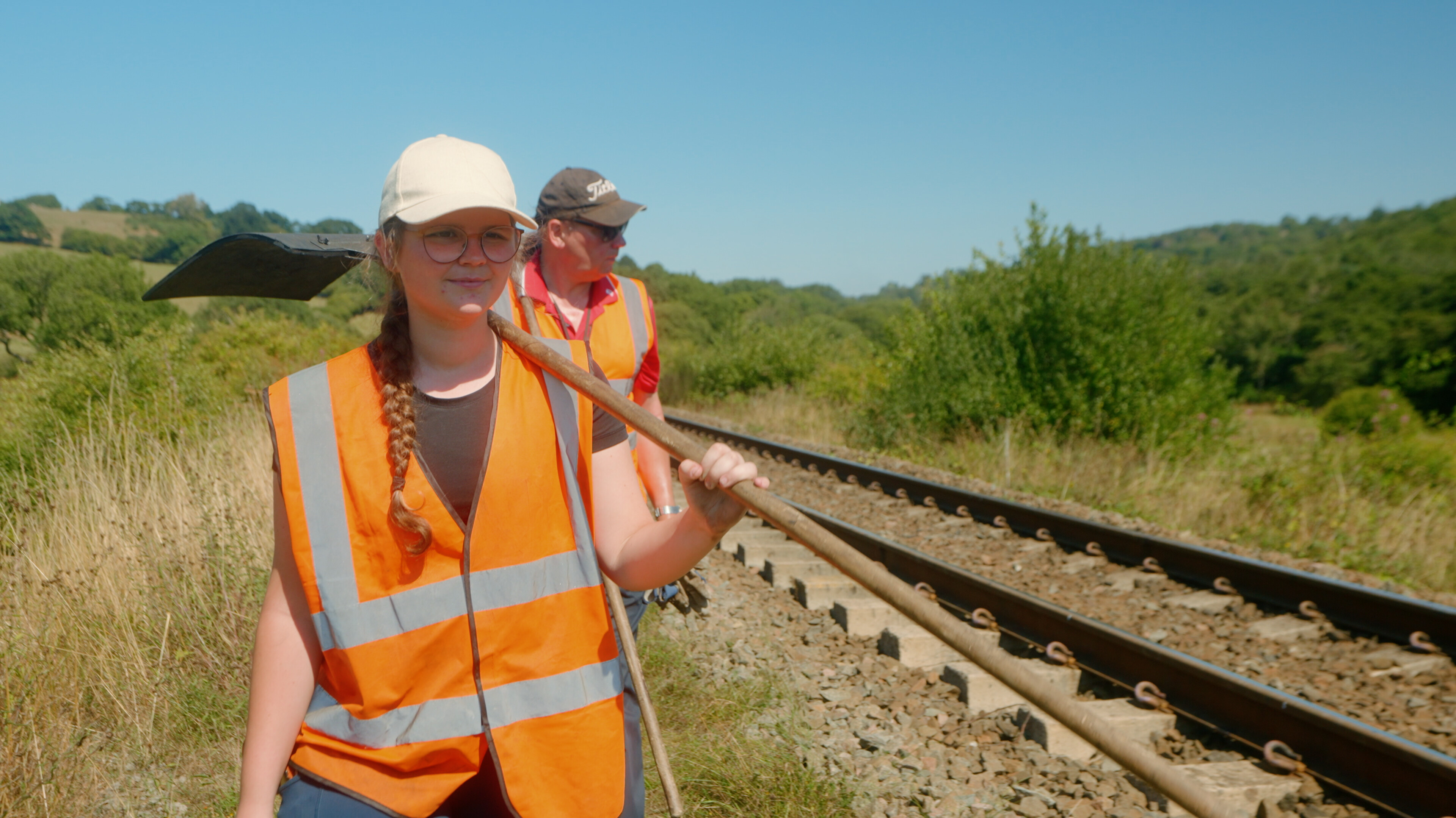 A lineside conservation volunteer walks along the line with a fire-beater in hand.