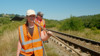 A lineside conservation volunteer walks along the line with a fire-beater in hand.