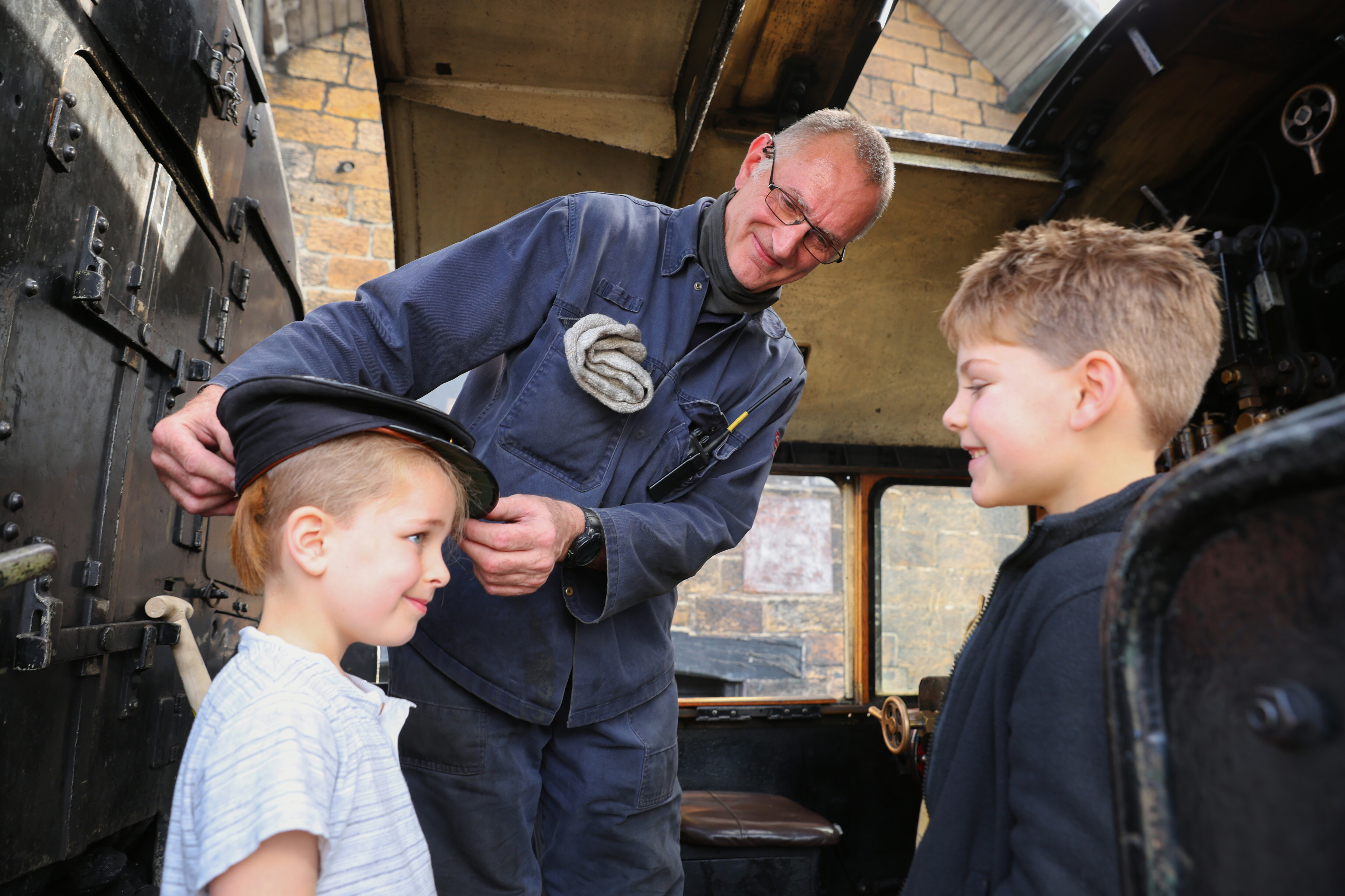 Two children try on the drivers hat on the footplate of a steam locomotive.