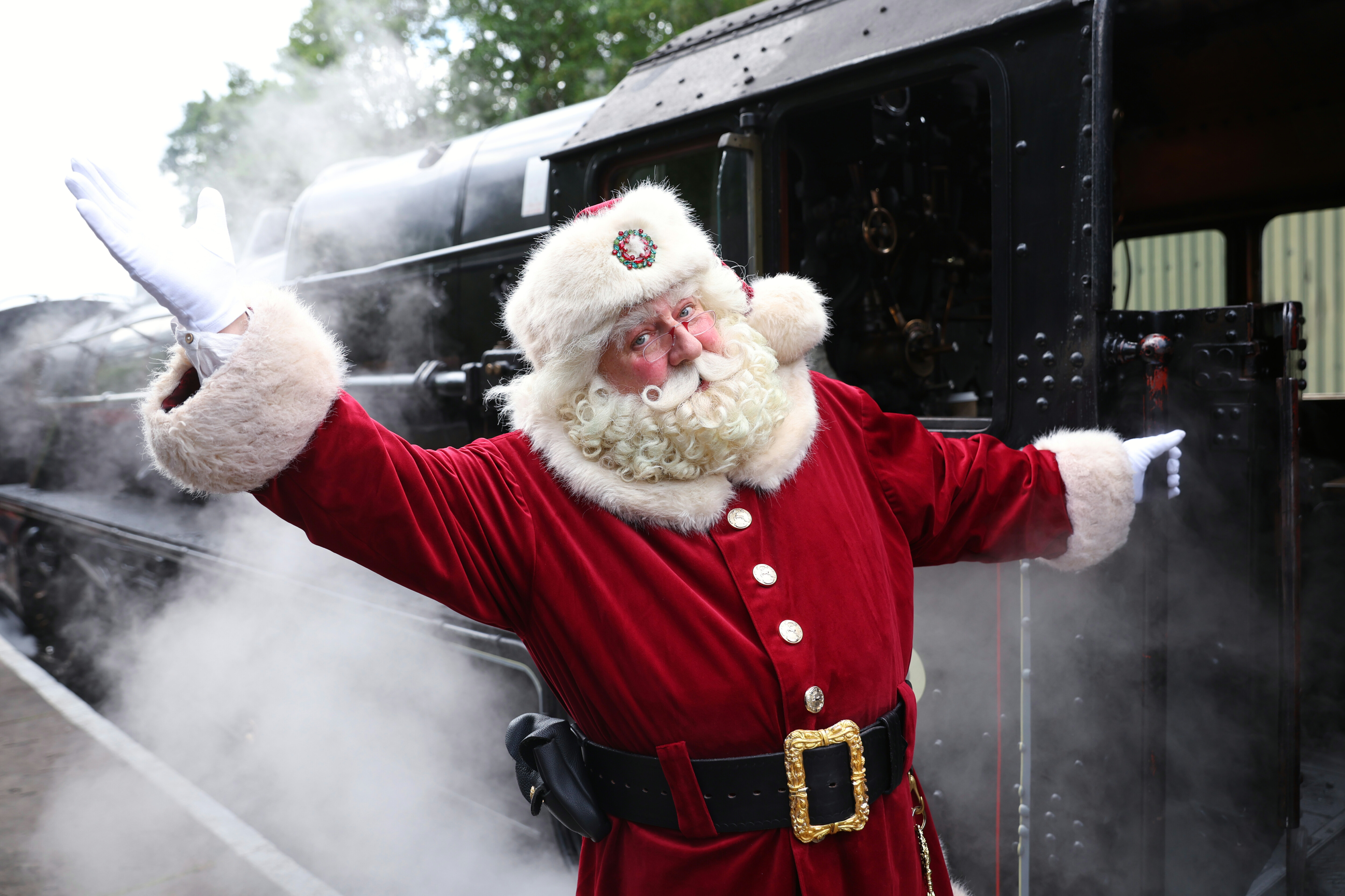 Santa with open welcoming arms in front of a steam locomotive.
