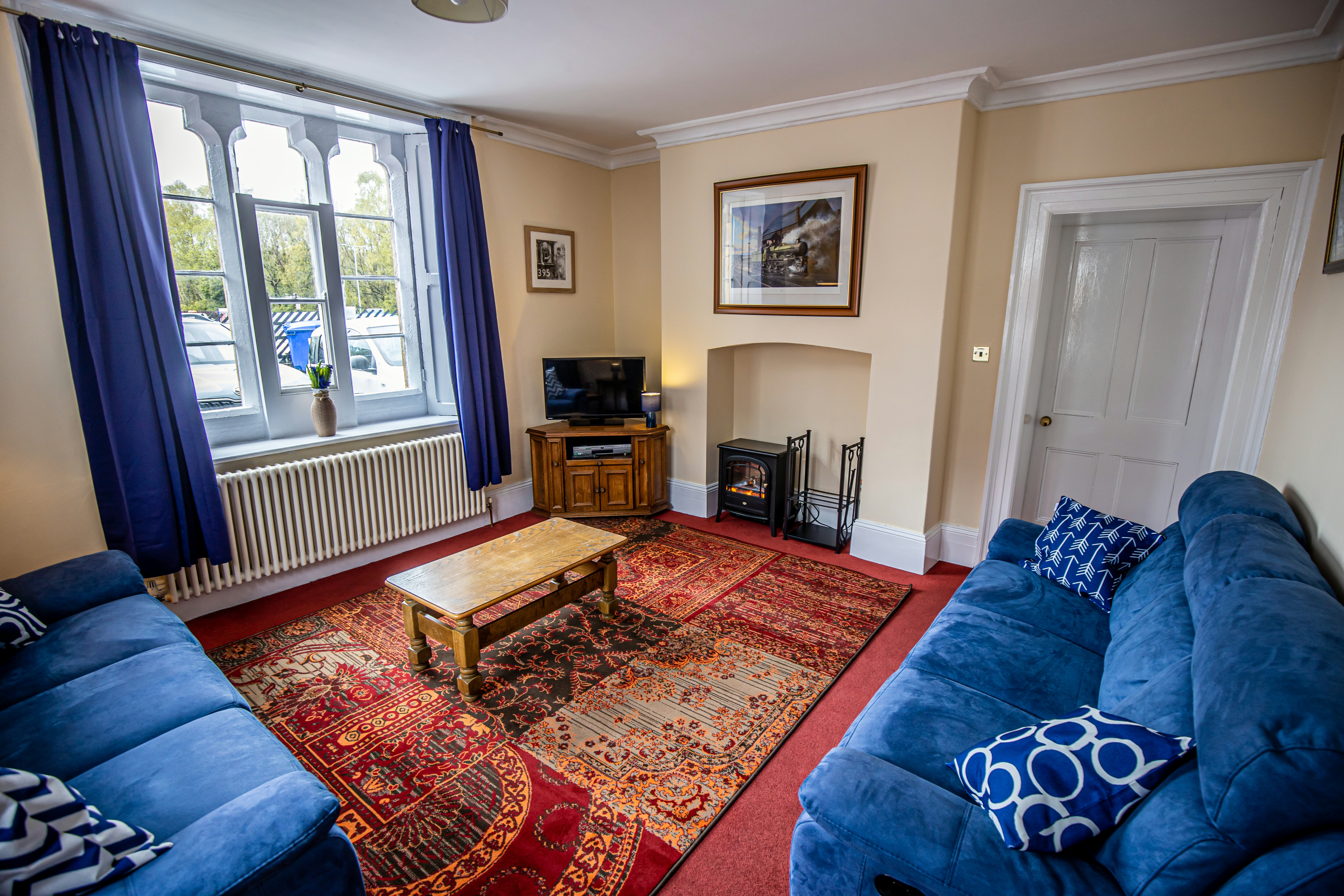 Grosmont Station House living room, with red carpets, blue furnishings and a flat-screen television.