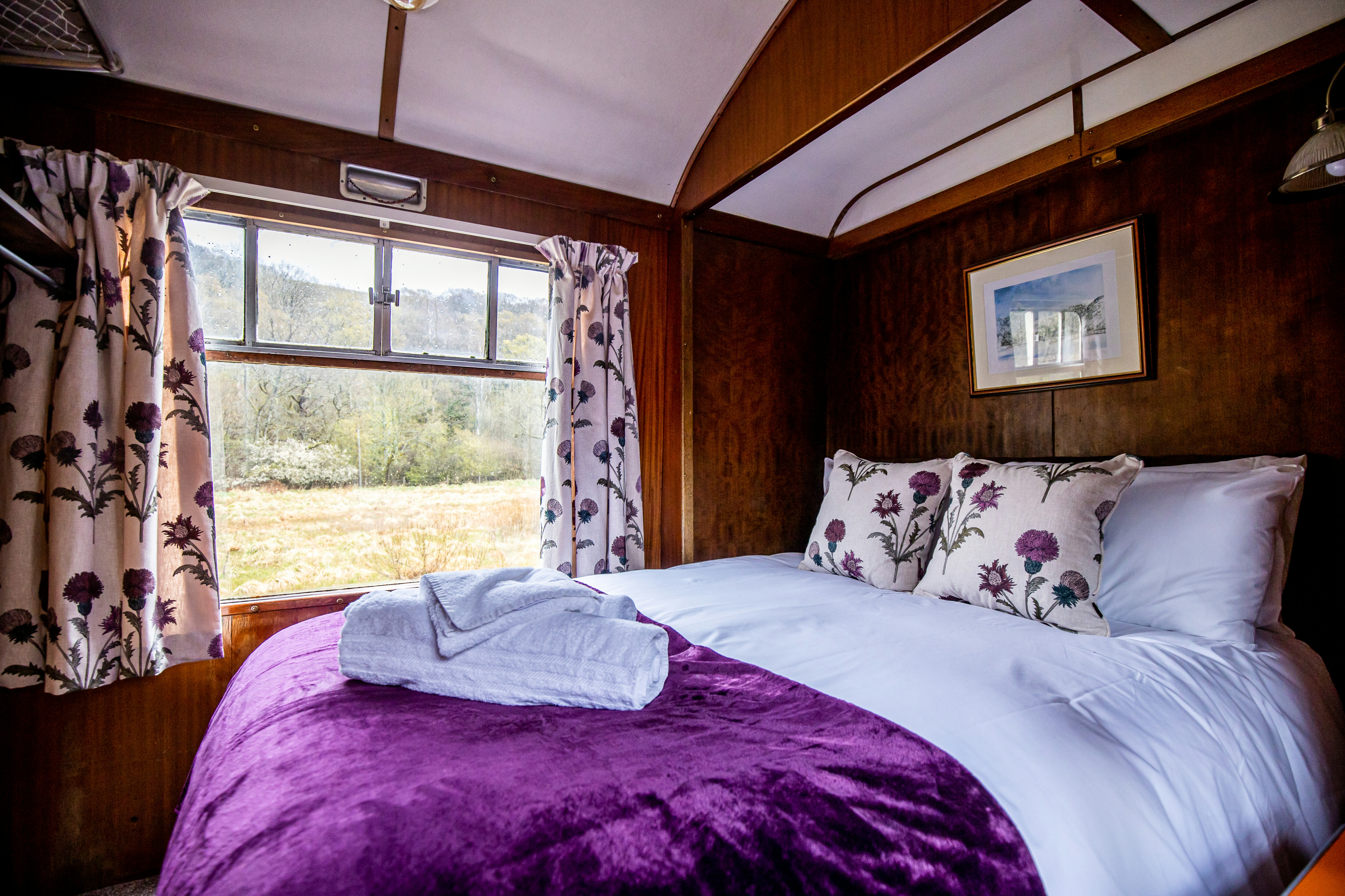 Levisham Camping Coach double bedroom with purple bedcover and views of the countryside out of the window.