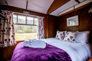Levisham Camping Coach double bedroom with purple bedcover and views of the countryside out of the window.